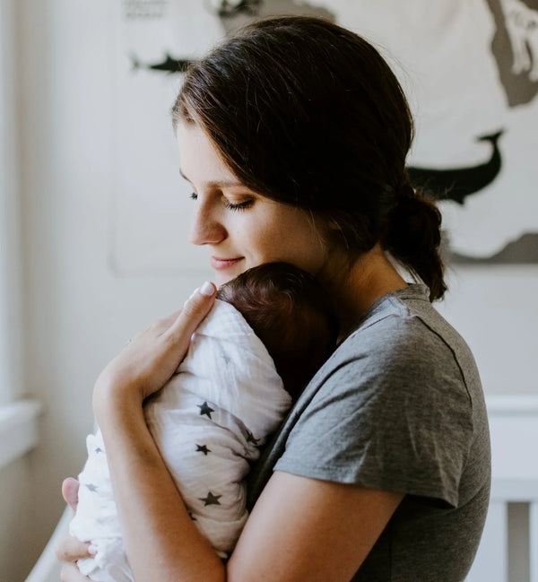 Mother holding and cuddling her newborn baby wrapped in a star-patterned blanket, symbolizing care, bonding, and postpartum wellness